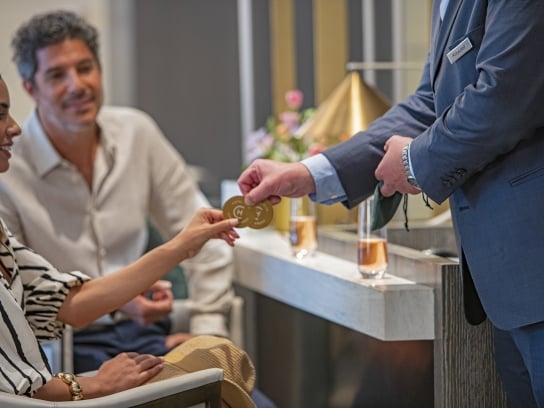 Event/meeting at Hotel Clio; A Man and woman at a meeting sitting and talking to a standing man wearing a blue suit.